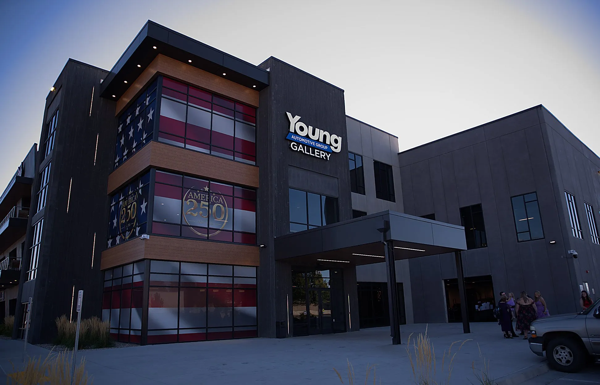 The Young Automotive gallery building at dusk, its flag-wrapped glass corner catching the last light
