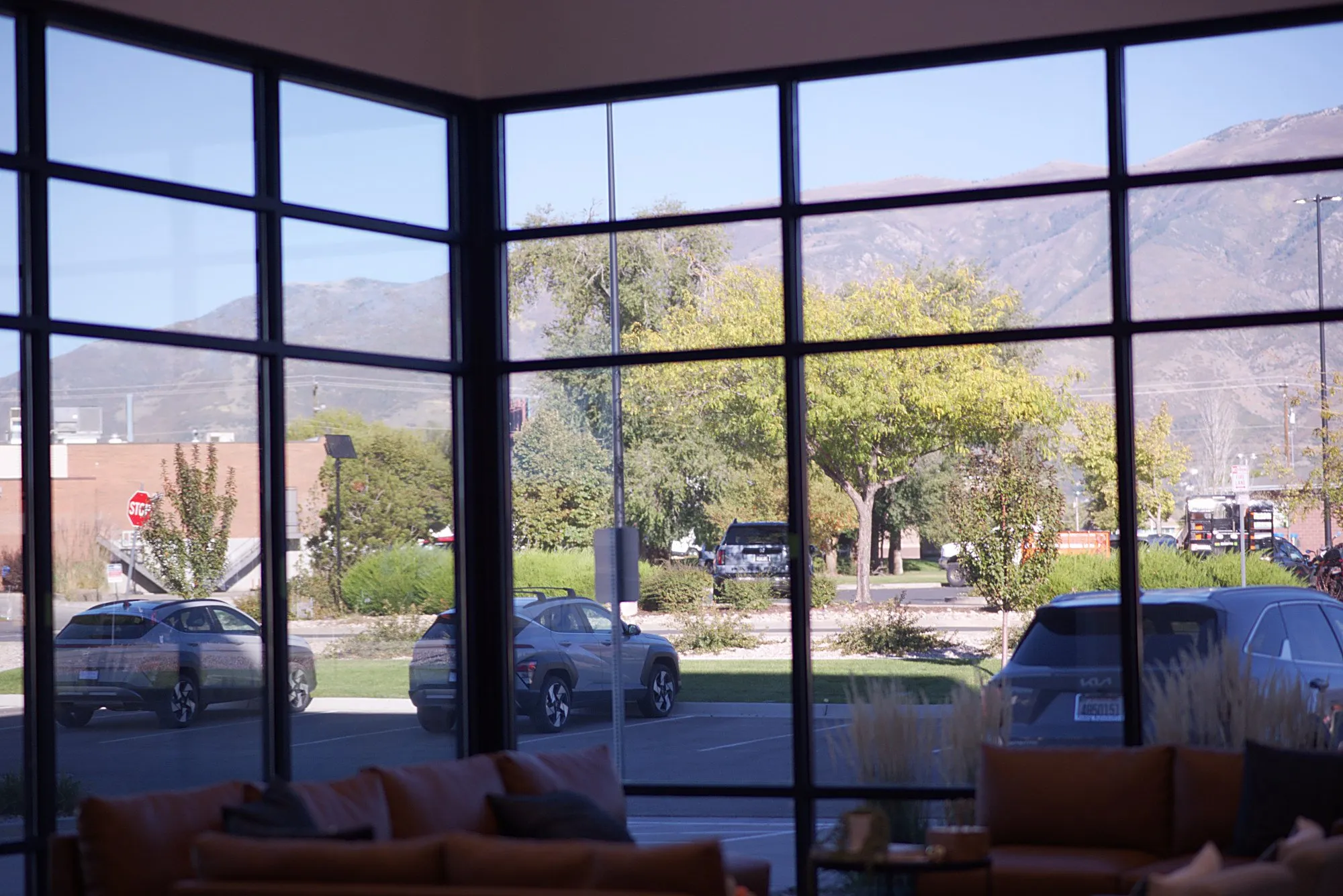 A leather lounge inside a glass corner, mountains and parked cars beyond the mullions