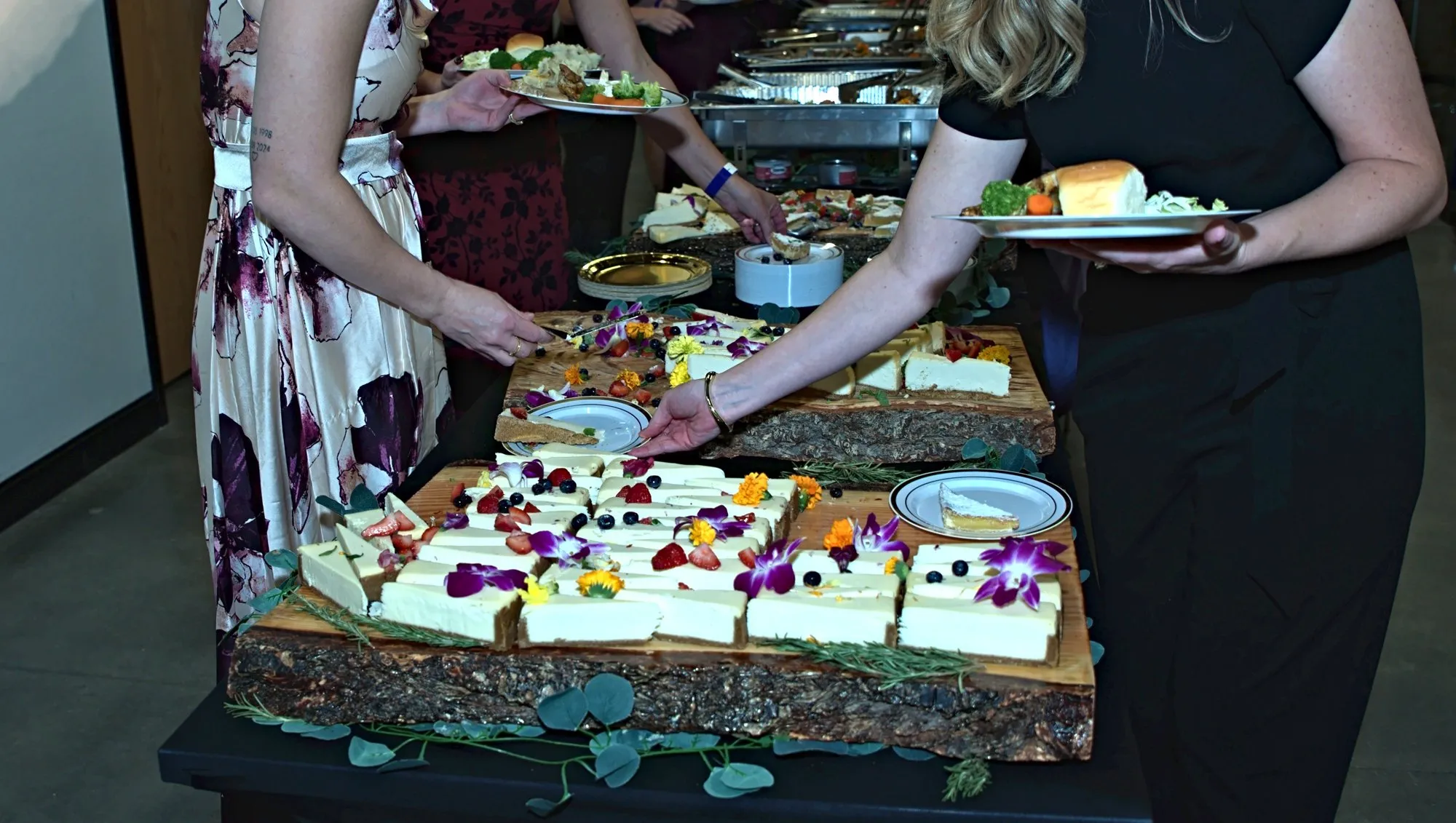 Guests in evening wear serving themselves cheesecake from the dessert board
