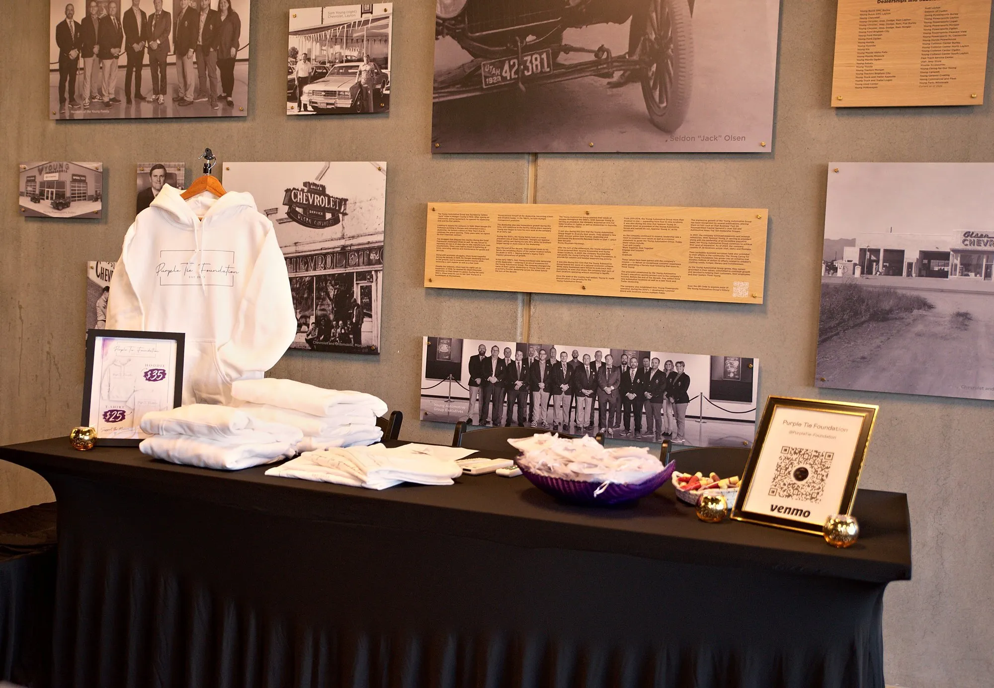 A history wall of archive prints above a table of folded white team jackets