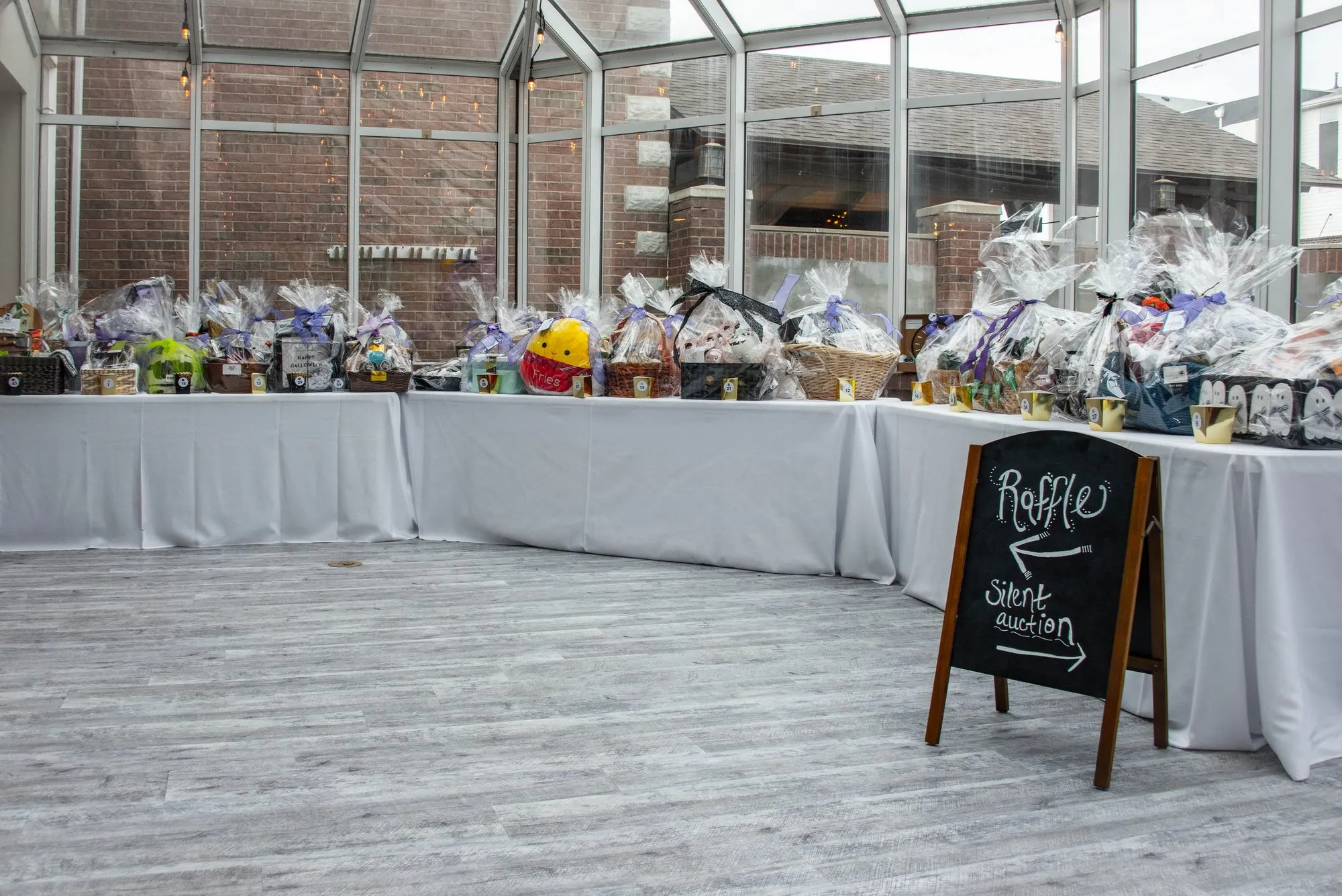Silent auction baskets lined up on a long table in a sunlit atrium