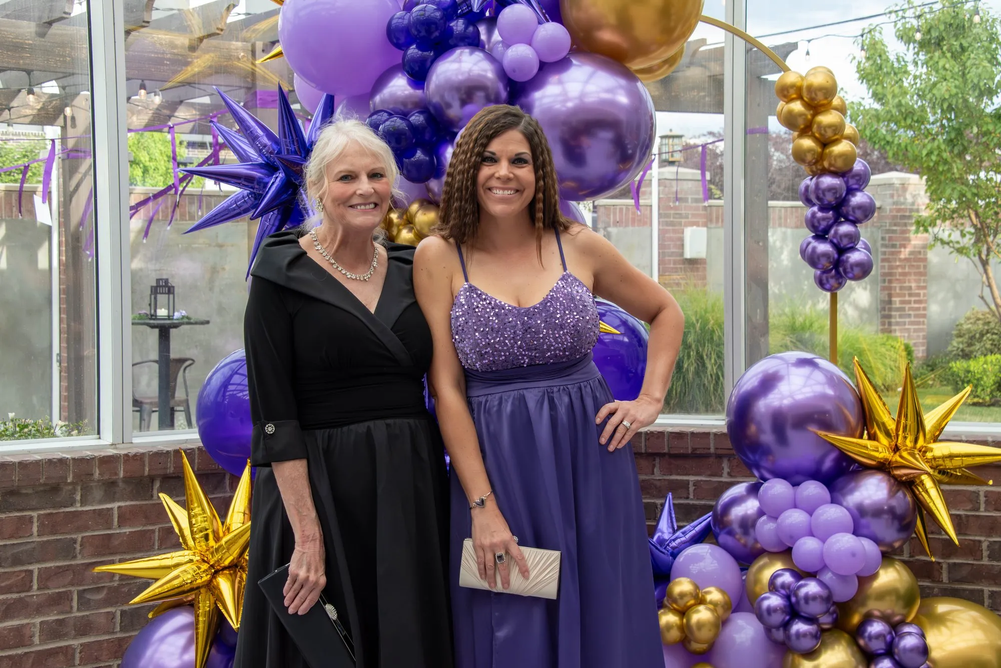 Two guests in evening wear laughing beside a purple and gold balloon installation