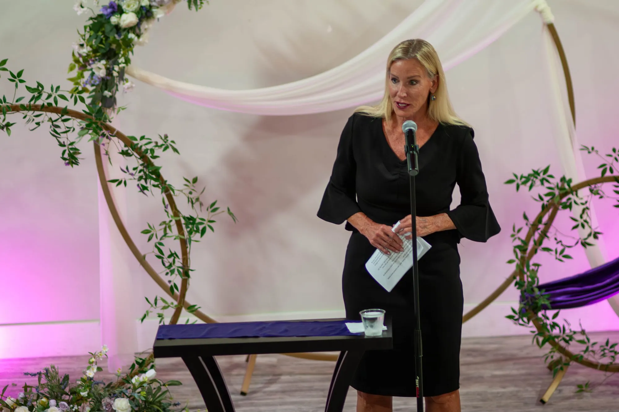 Emcee at the podium beneath a floral arch, addressing gala guests