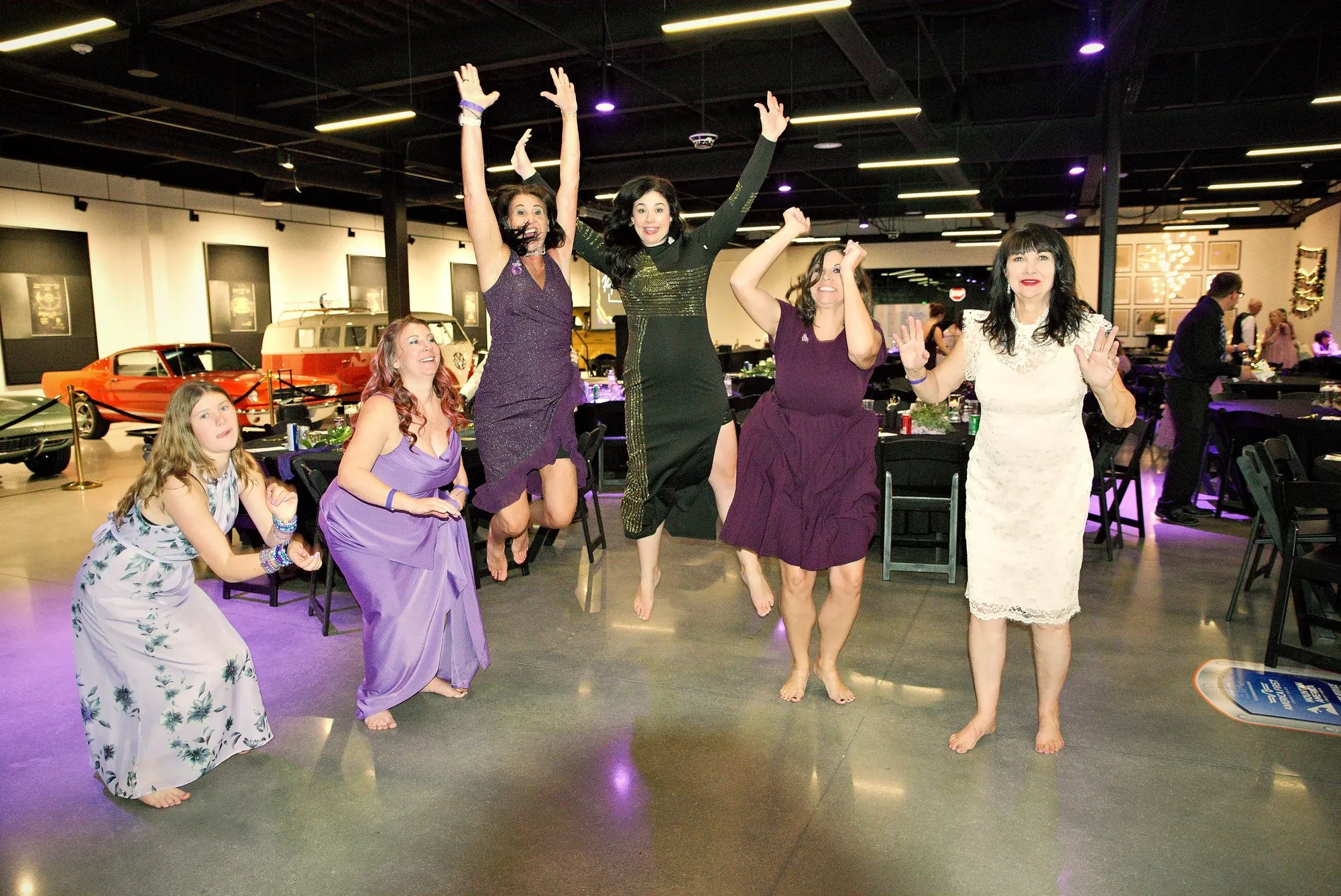 Gala guests leaping into the air on the dance floor with classic cars behind them