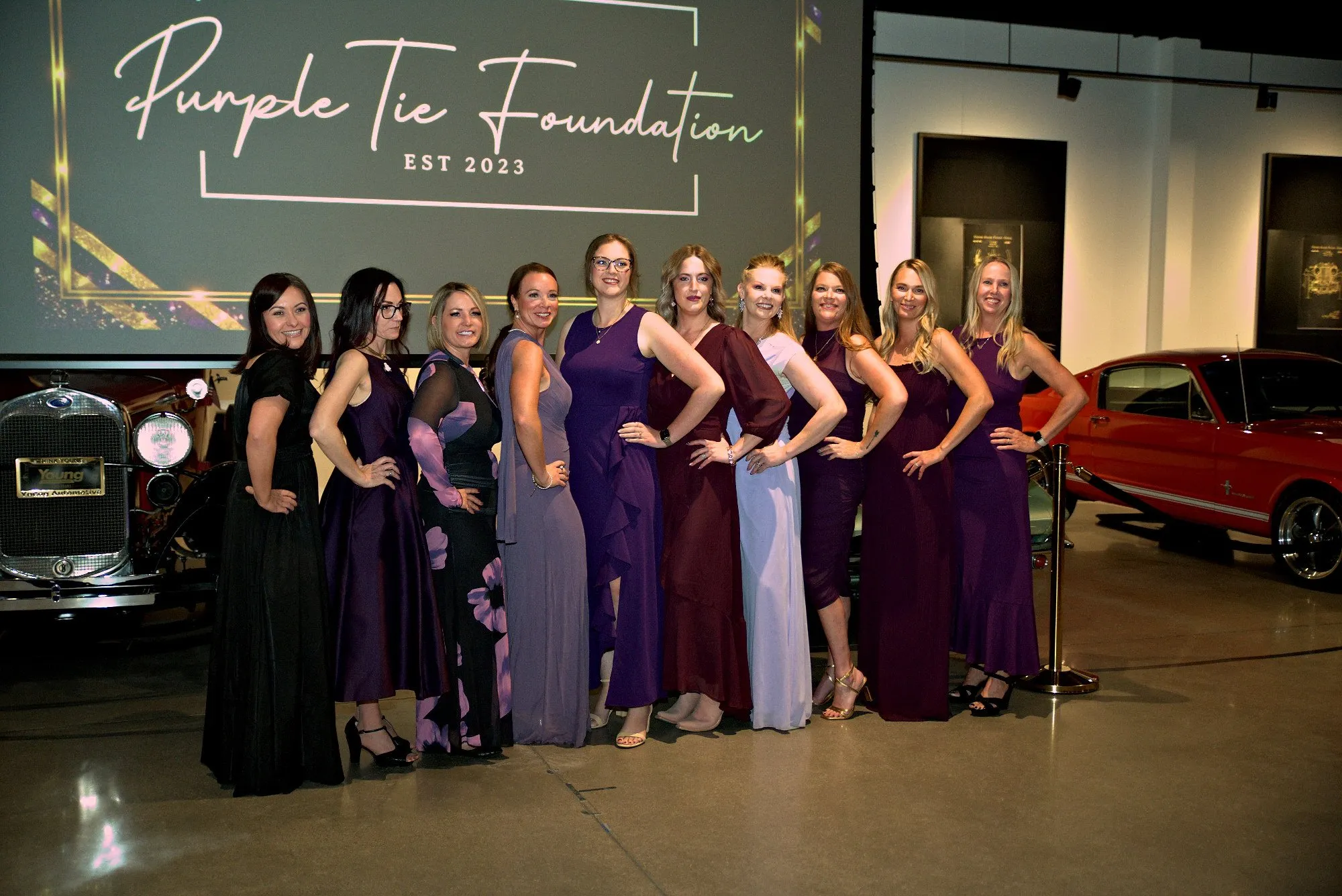 The foundation team lined up under a projected logo beside a red classic car