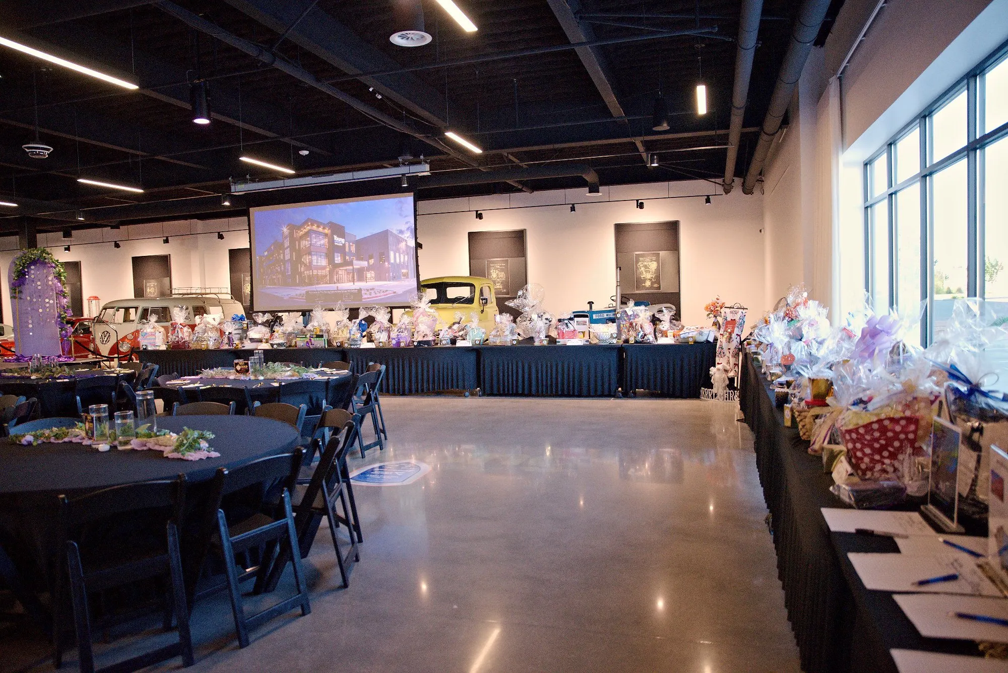 The Purple Tie Gala room set before doors open, with a vintage VW bus beside the auction table under the ceiling lights