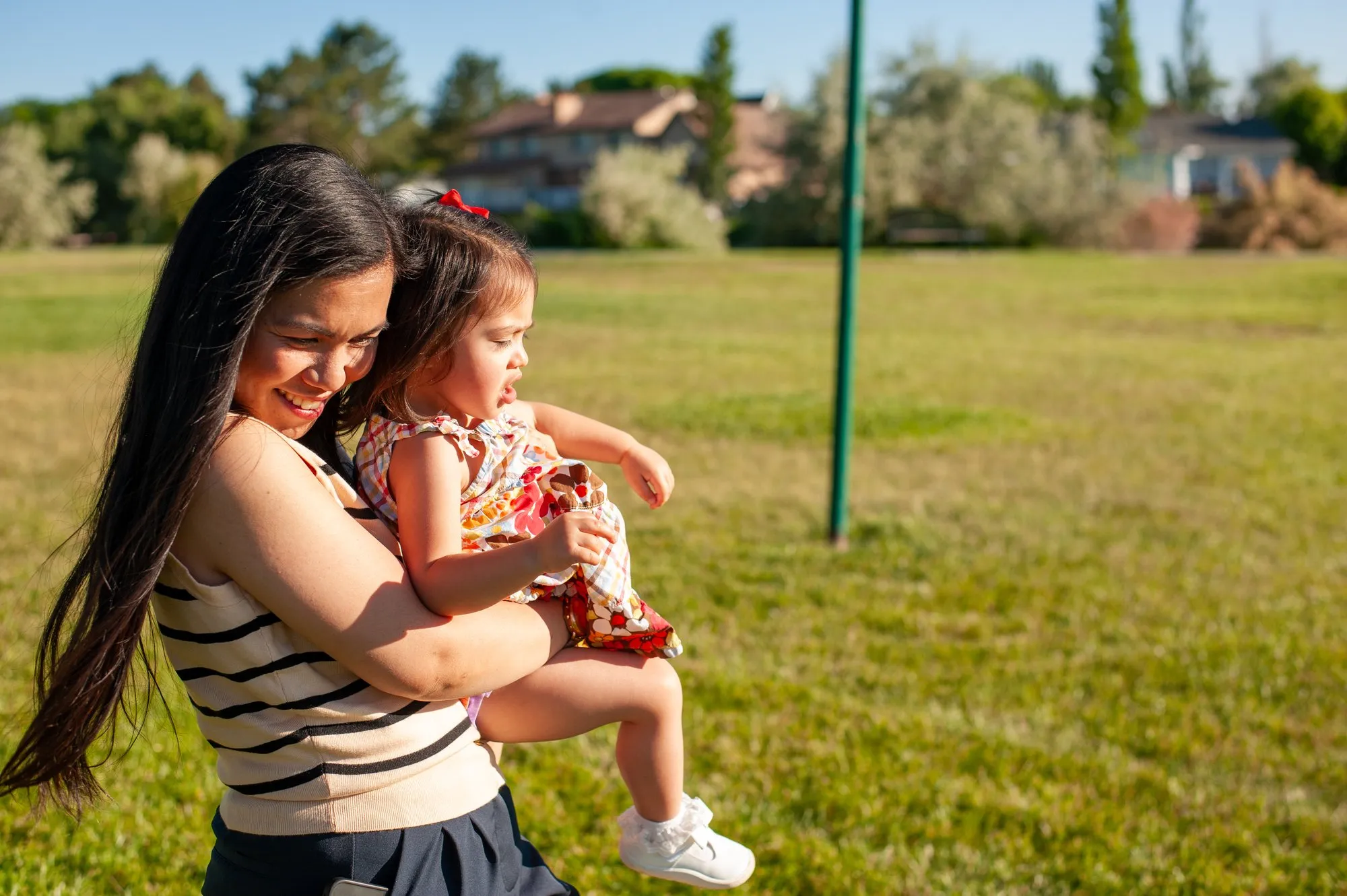 Mother holding her young daughter close on a sunlit lawn