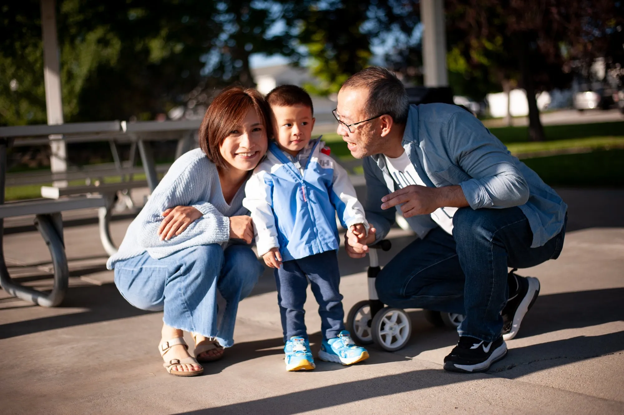 Father and grandfather crouched beside a toddler on his balance bike