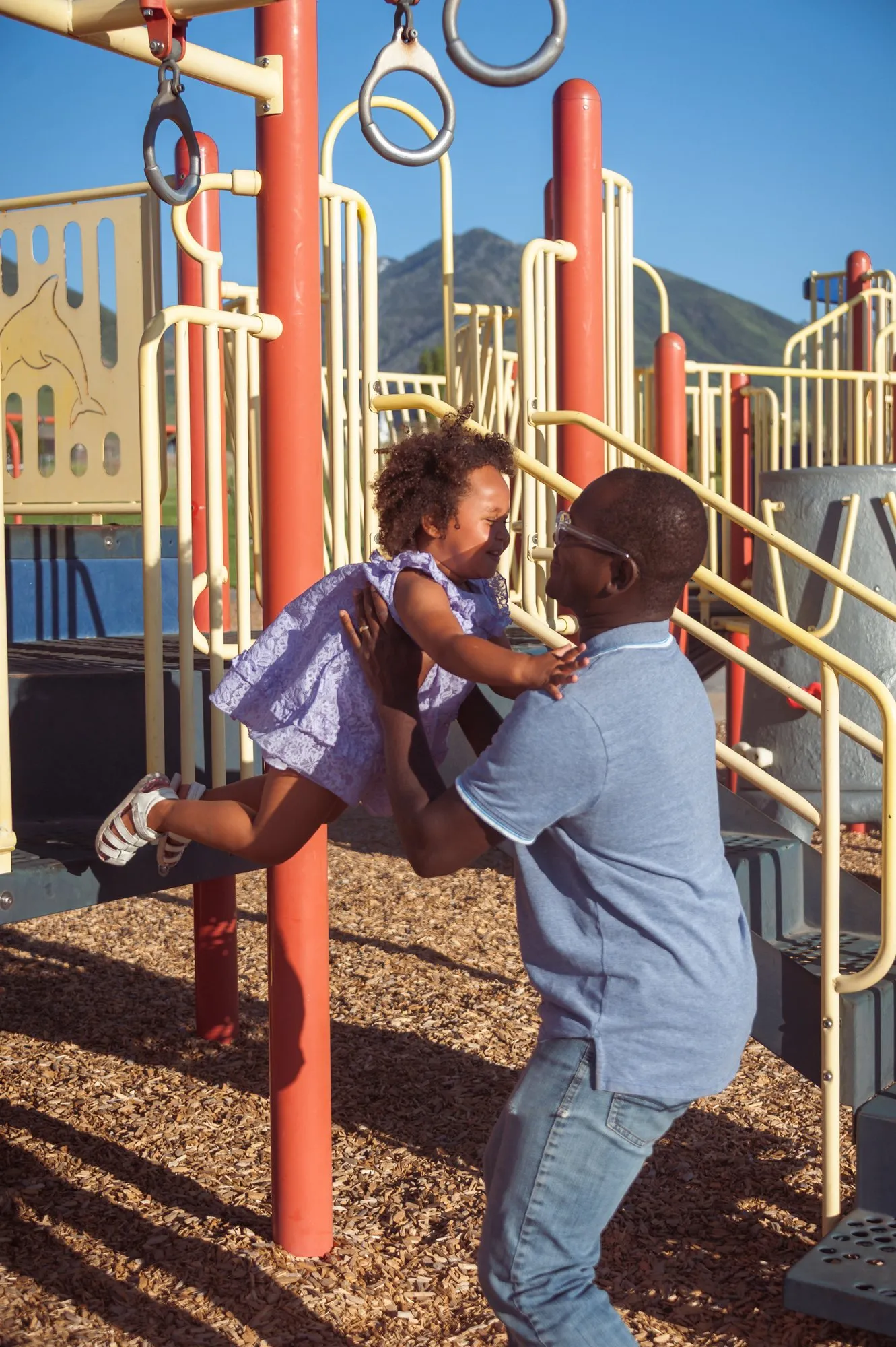 Father swinging his laughing toddler on a playground climbing frame