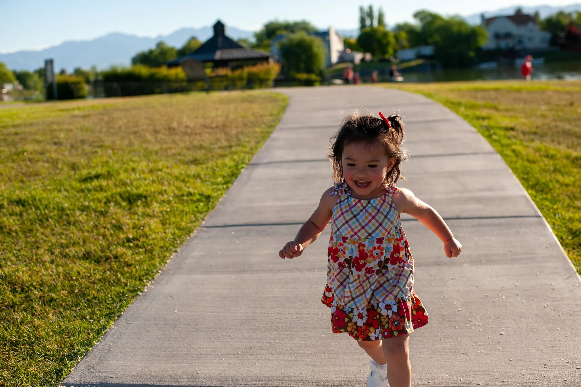 Little girl in a floral dress running down a park path toward the camera