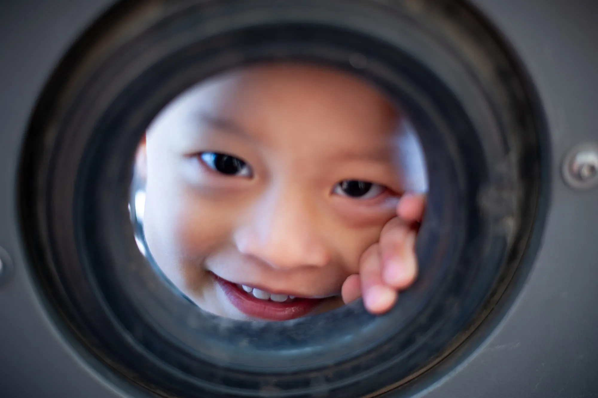 Small boy grinning through a playground tunnel window