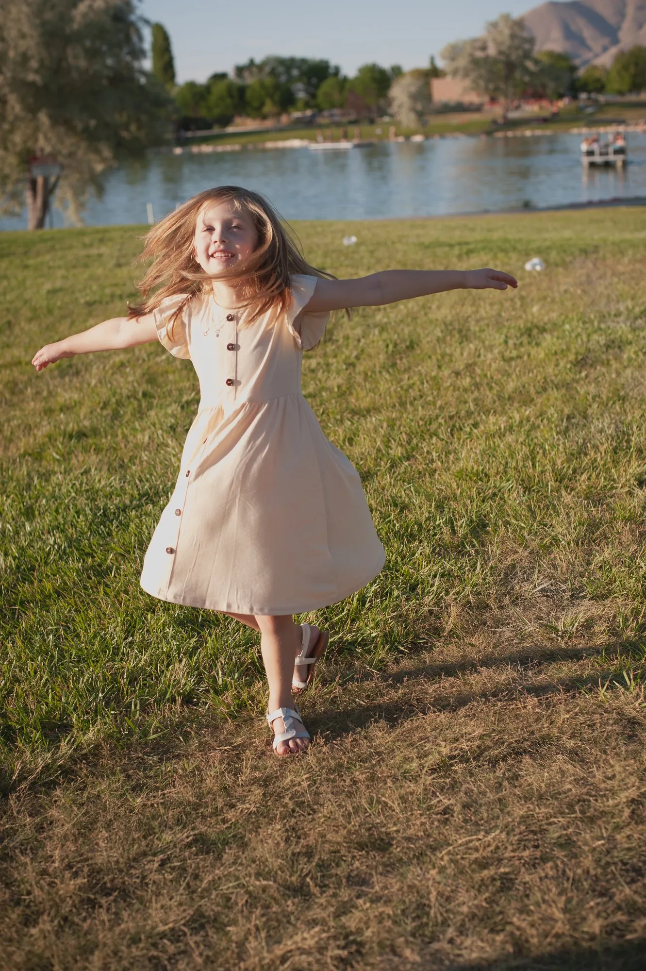 Girl in a cream dress twirling on the grass, arms out