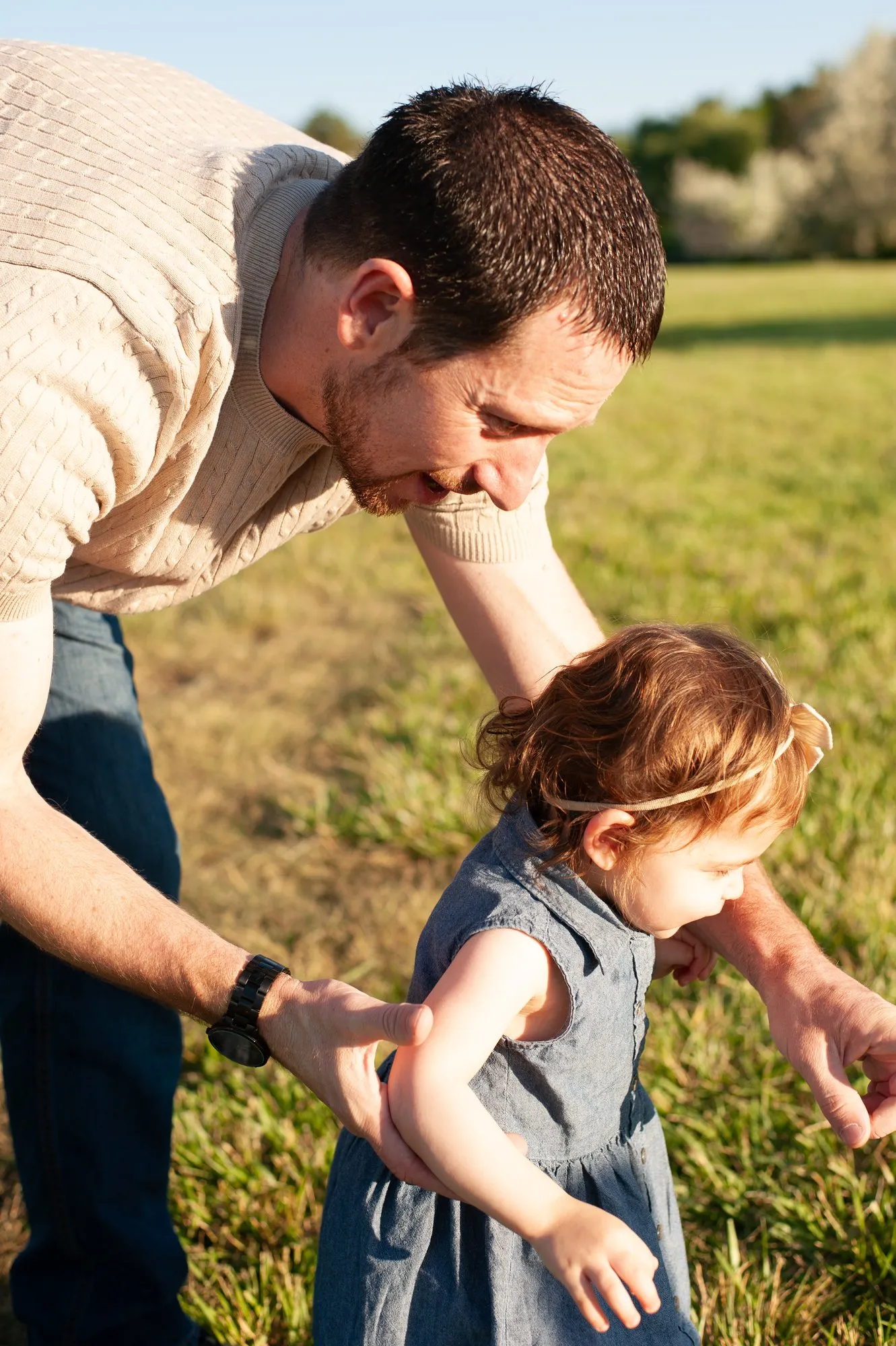 Father leaning down to hold his toddler daughter's hand as she walks