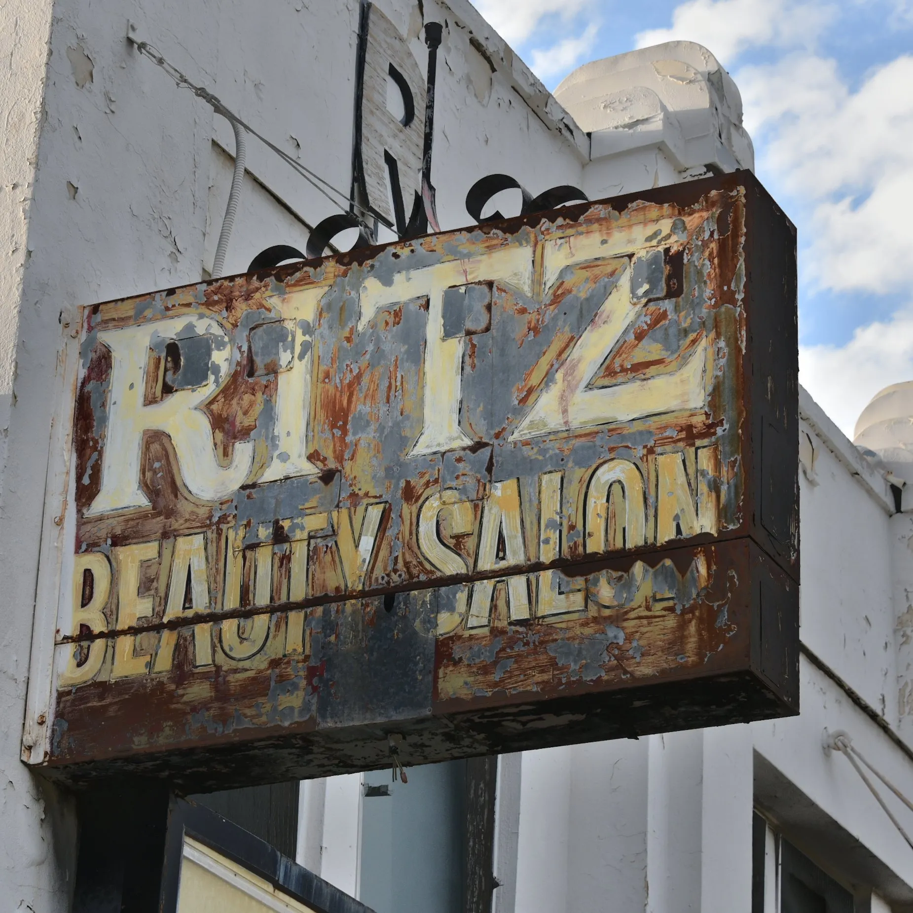 Rusted vintage Ritz Beauty Salon sign against a cloudy sky