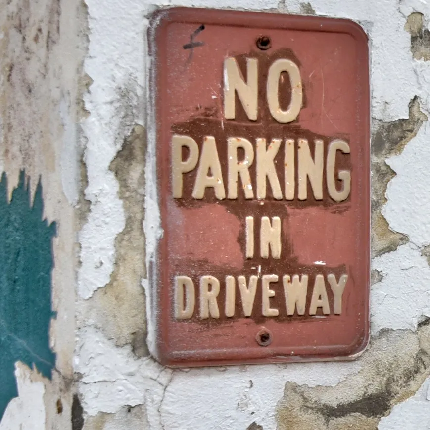 Faded No Parking sign on a cracked stucco wall